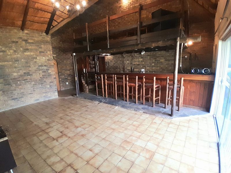 Rustic entertainment area featuring a built-in bar, exposed brick walls, timber mezzanine loft, and high vaulted ceilings with exposed trusses.