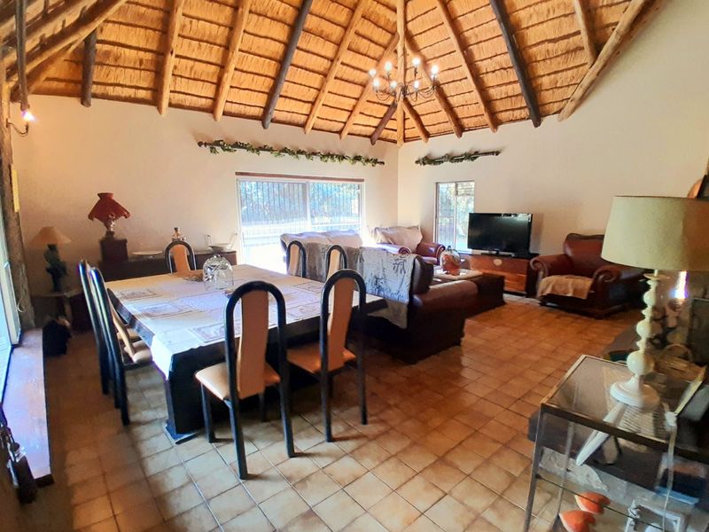 Spacious open-plan living and dining area featuring a high vaulted thatched ceiling with exposed timber rafters and ceramic tiled flooring.