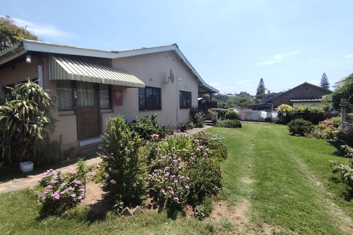 Rear view of the property featuring a landscaped garden, lawn area, and a covered patio section with a retractable awning.