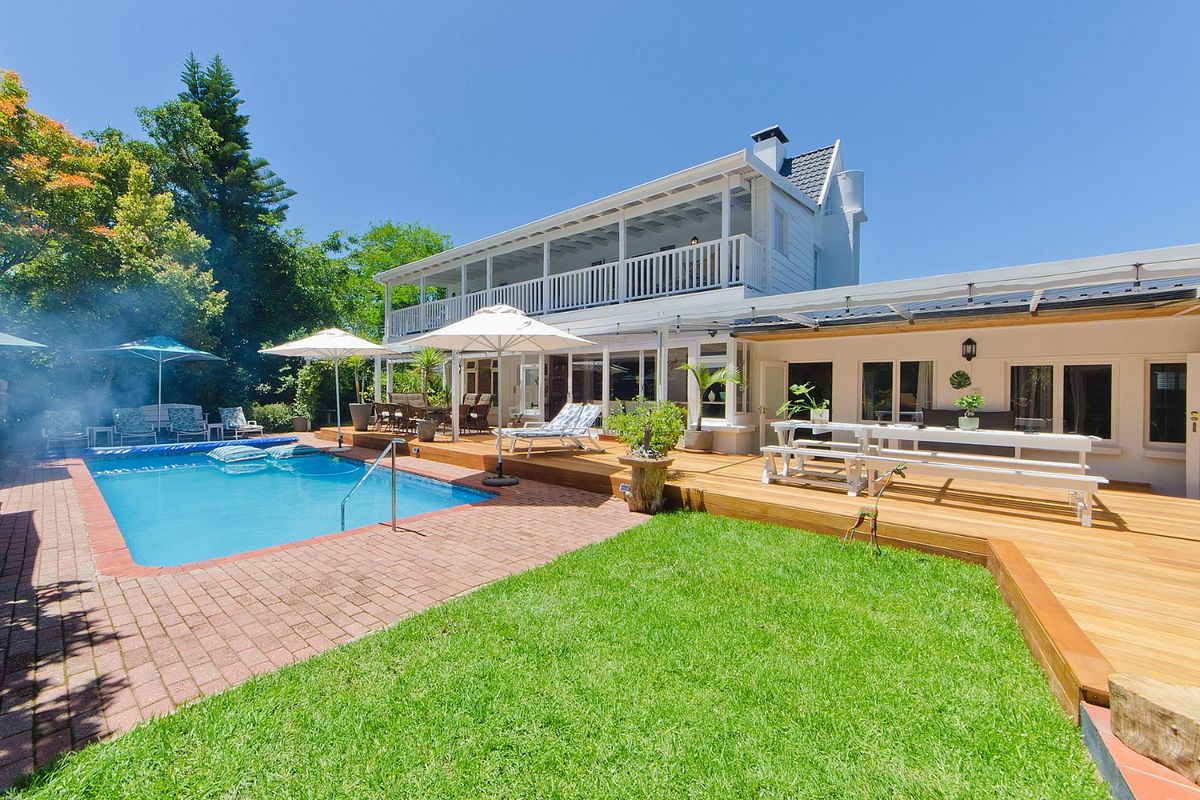 Spacious rear garden featuring a swimming pool, extensive timber decking, and a covered patio area attached to the two-story residence.