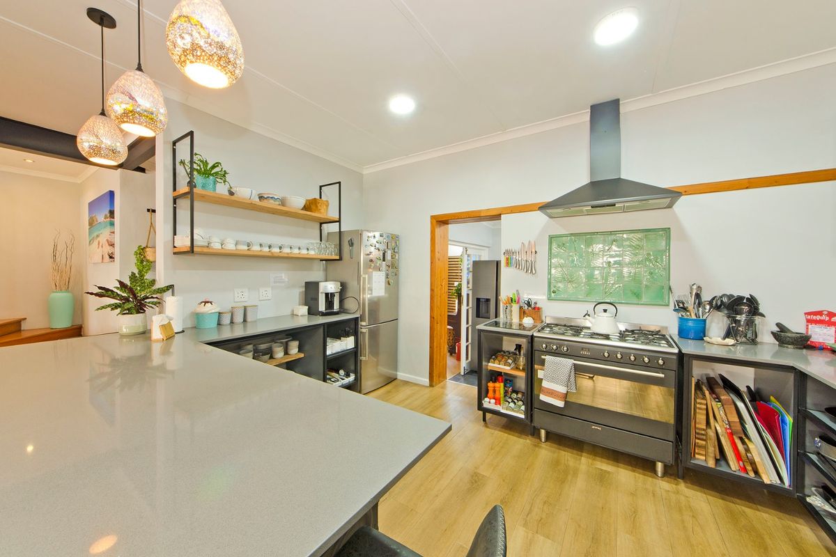 Modern kitchen featuring a large stone island, gas range cooker with extractor hood, open shelving, and durable laminate flooring.