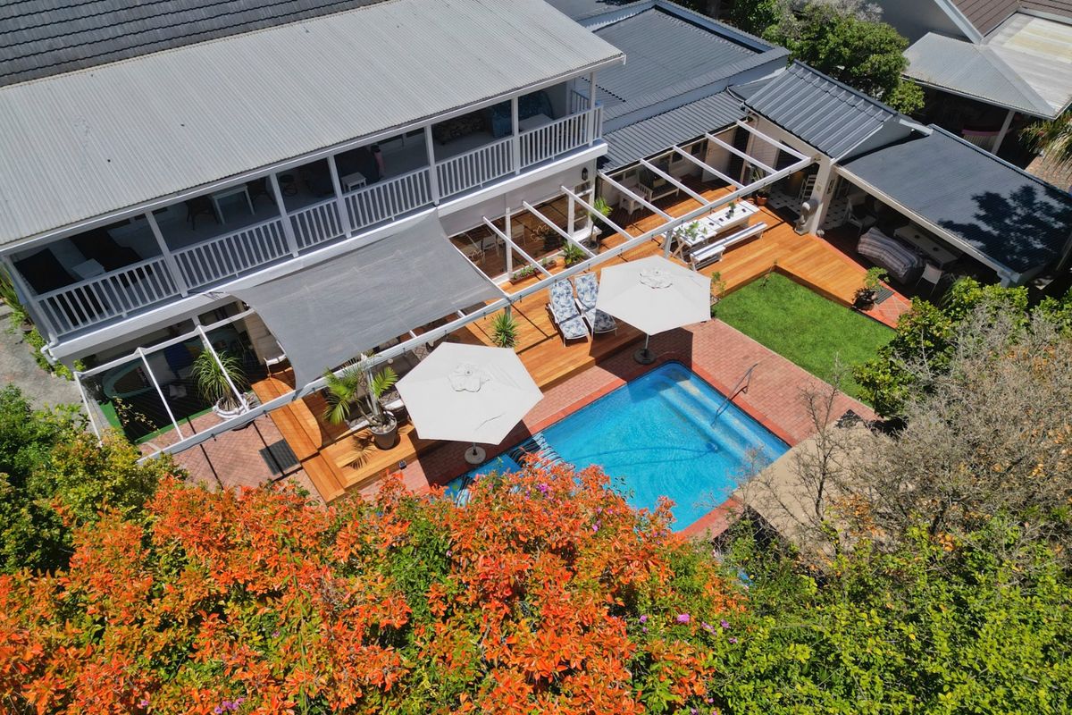 Aerial view of a well-maintained property featuring a swimming pool, expansive timber decking, brick paved areas, and a covered balcony.