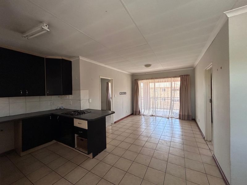An open-plan kitchen and living area featuring tiled floors, built-in cabinetry with a hob, and access to a balcony through sliding glass doors.