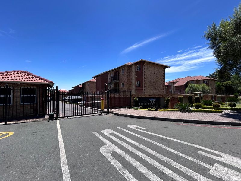 Street view of the apartment complex entrance featuring a secure gated access point, brick building facades, and well-maintained landscaping.