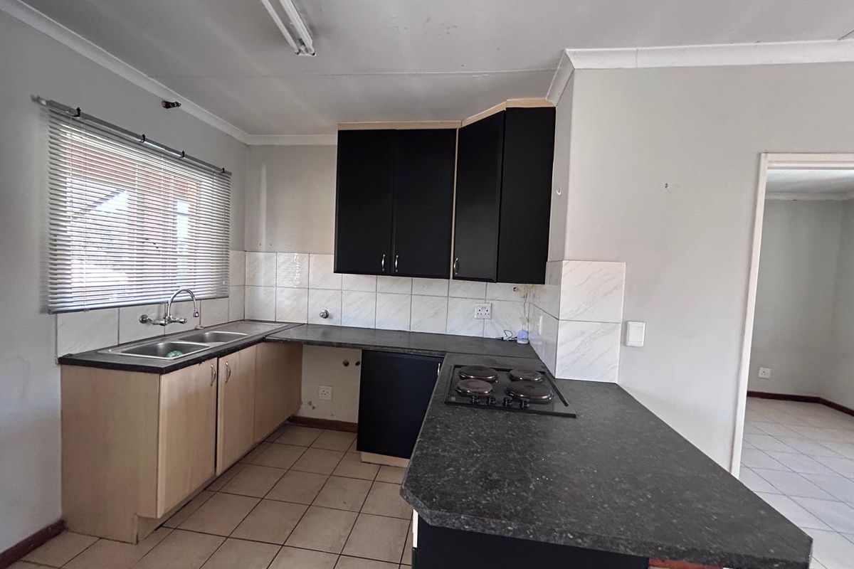 A functional kitchen featuring built-in cabinetry, laminate countertops, a double basin sink, and an integrated electric hob with tiled backsplash and flooring.