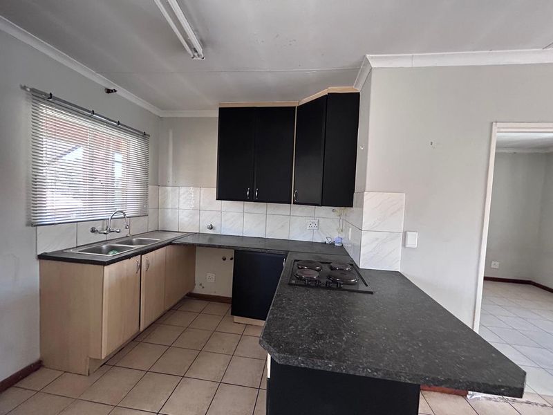 A functional kitchen featuring built-in cabinetry, laminate countertops, a double basin sink, and an integrated electric hob with tiled backsplash and flooring.