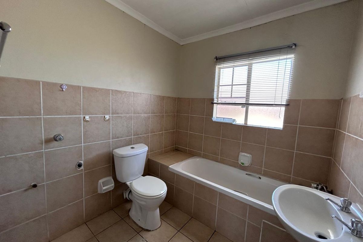A functional bathroom featuring a bathtub, pedestal basin, and toilet, finished with neutral wall and floor tiles. Requires minor fixture repairs.