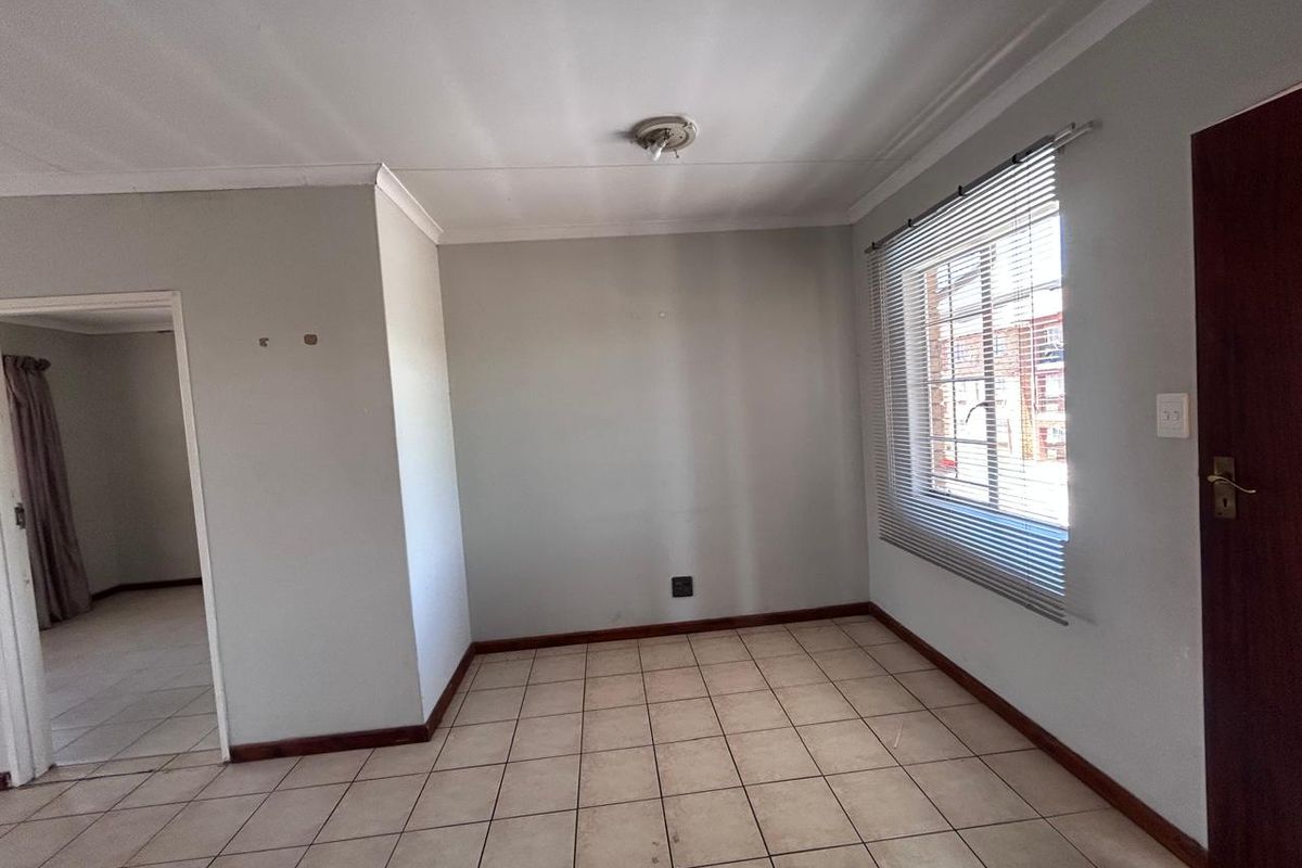 An empty living room featuring neutral tiled flooring, coved ceilings, and a window fitted with venetian blinds, offering a blank canvas for personalization.