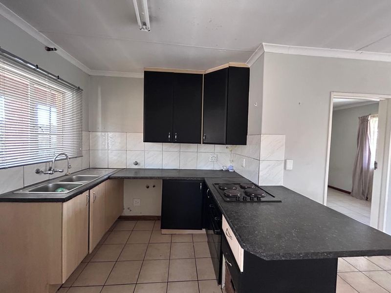 A functional kitchen featuring dark cabinetry, laminate countertops, a built-in hob and oven, and tiled flooring, offering a blank canvas for renovation.