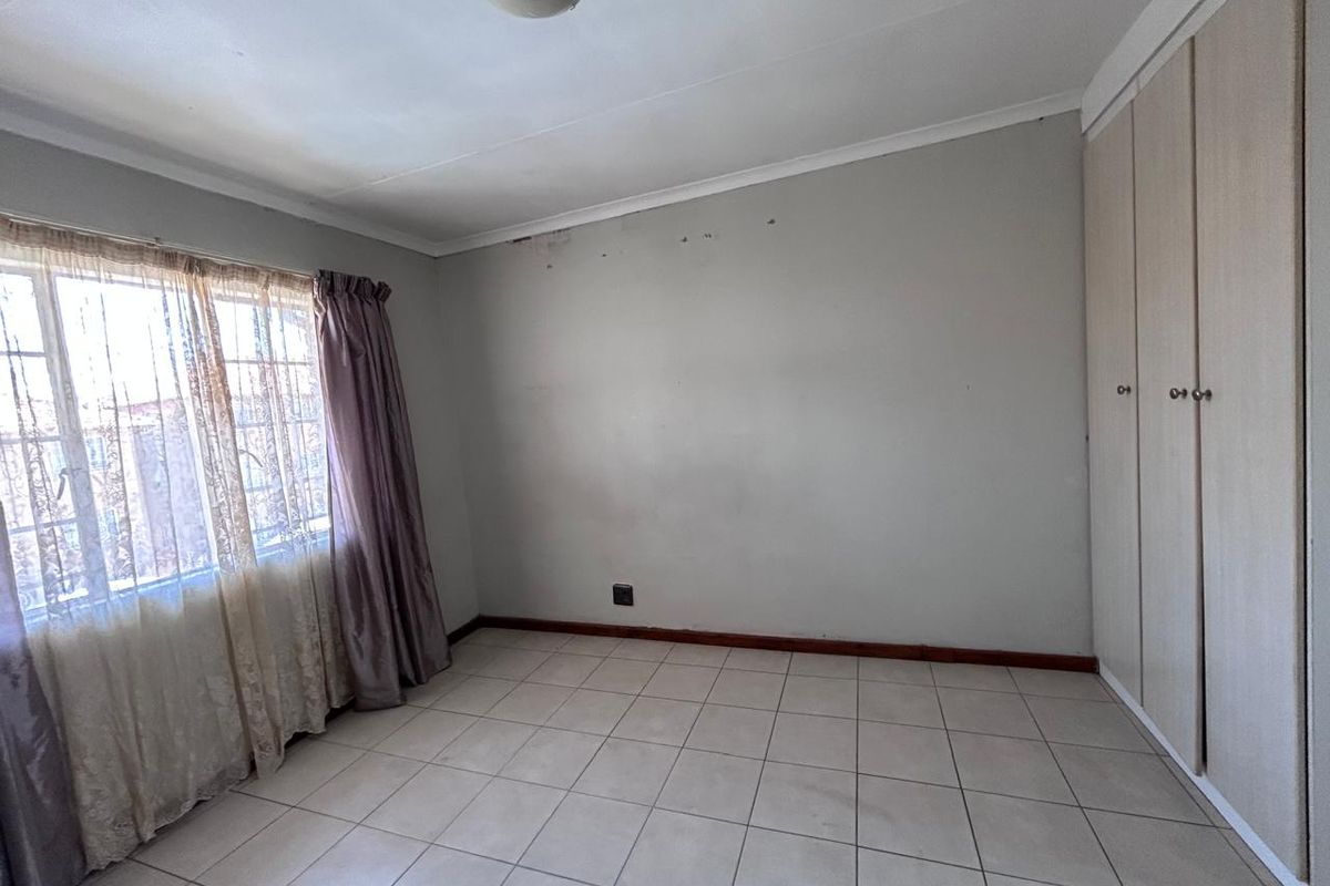 An empty bedroom featuring tiled flooring, built-in cupboards, and a window with curtains. The room requires minor cosmetic attention to the walls and ceiling.
