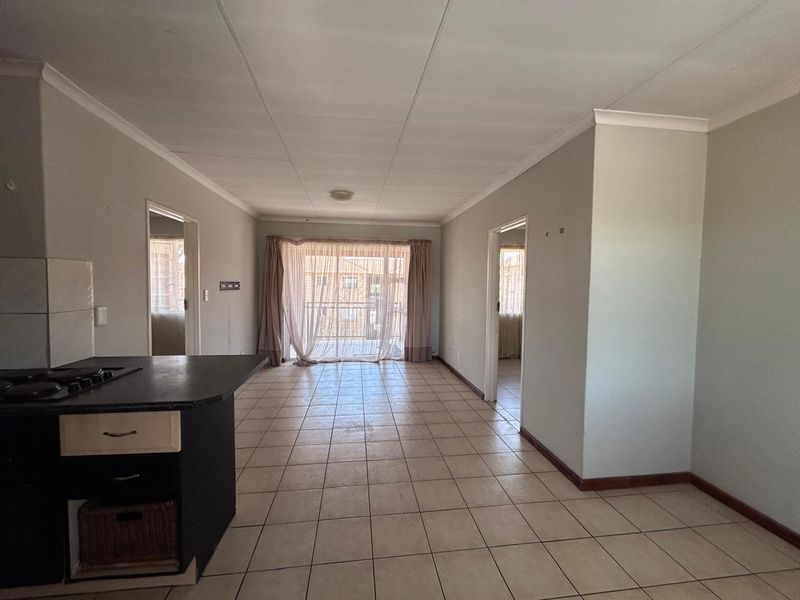 Spacious open-plan living and kitchen area featuring tiled flooring, a built-in kitchen counter with hob, and access to a balcony through sliding glass doors.