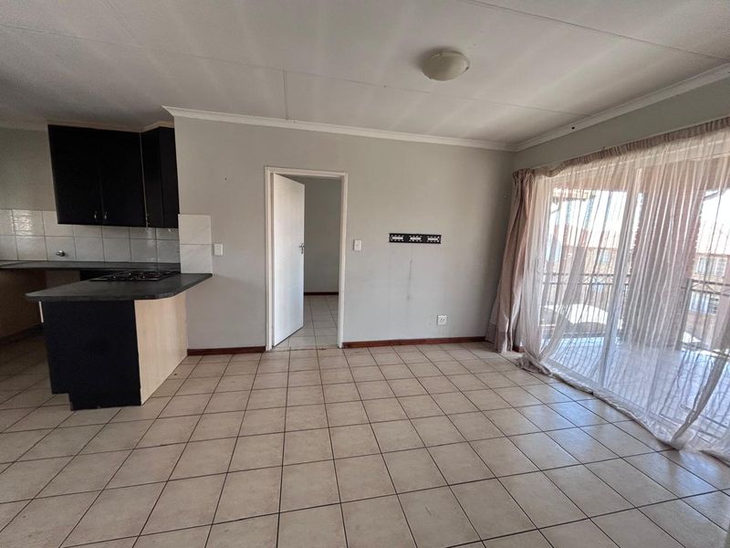 An open-plan living and kitchen area featuring tiled flooring, built-in cabinetry with a hob, and a sliding door leading to a balcony.
