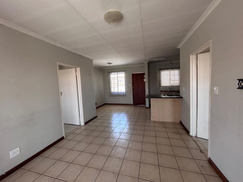 An open-plan living and kitchen area featuring tiled flooring, a breakfast bar, and neutral wall finishes, presenting a blank canvas for potential updates.
