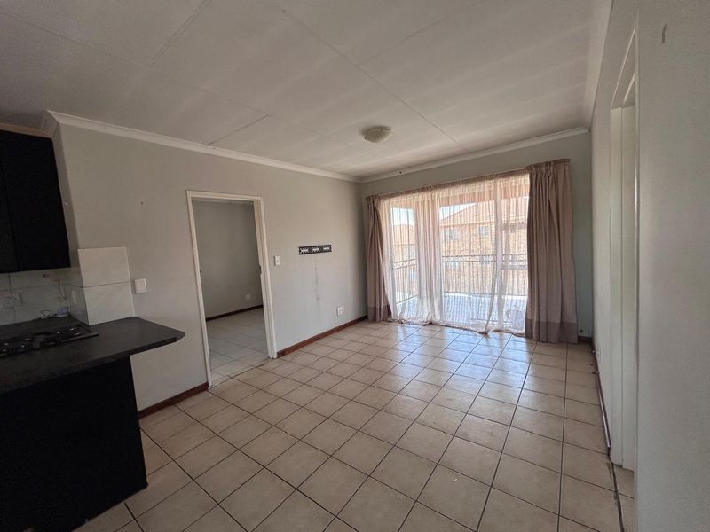 Open-plan living area featuring tiled flooring, a compact kitchen corner, and a sliding door leading to a balcony.