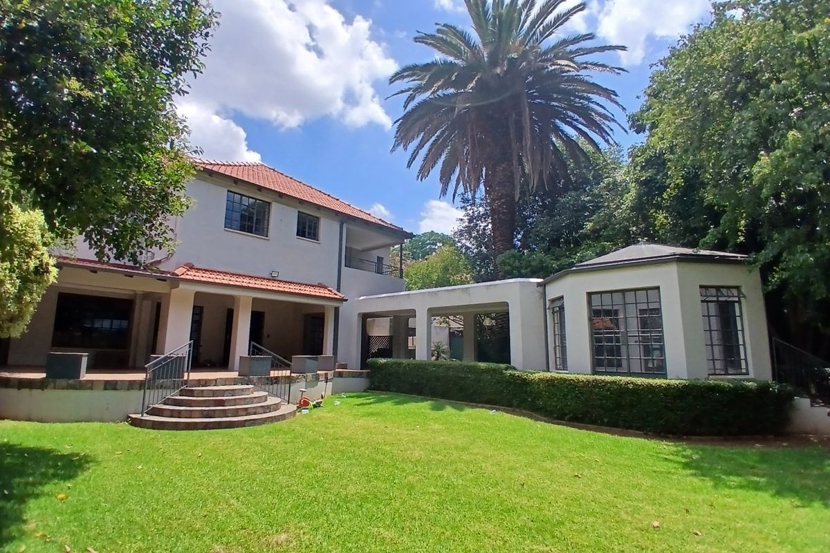 Rear view of the property featuring a spacious lawn, established garden, covered patio area, and a classic two-story architectural design with terracotta roof tiles.
