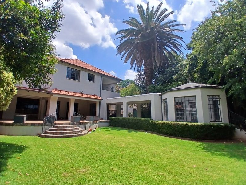 Rear view of the property featuring a spacious lawn, established garden, covered patio area, and a classic two-story architectural design with terracotta roof tiles.