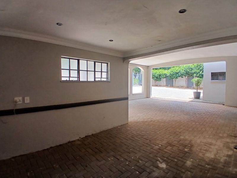 A spacious, empty garage featuring paved flooring, recessed downlighting, and an open archway leading to the exterior driveway area.