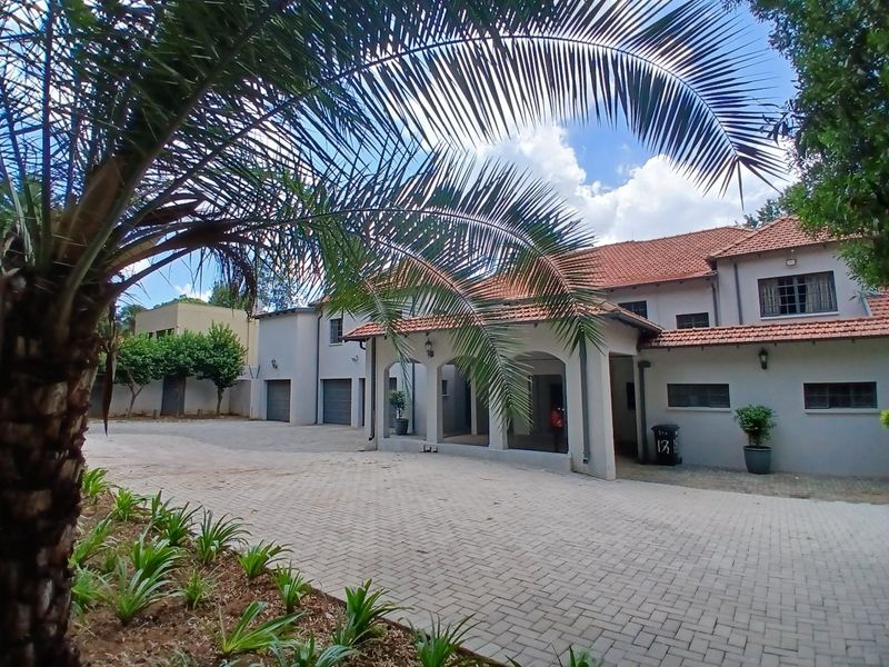 Front elevation of a multi-story residence featuring a paved driveway, covered entrance porch, and tiled roof, set within a landscaped property.