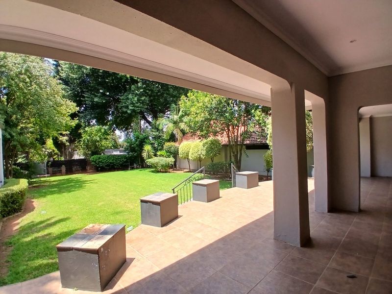 A spacious covered patio featuring tiled flooring and concrete pillars, overlooking a well-maintained garden area.
