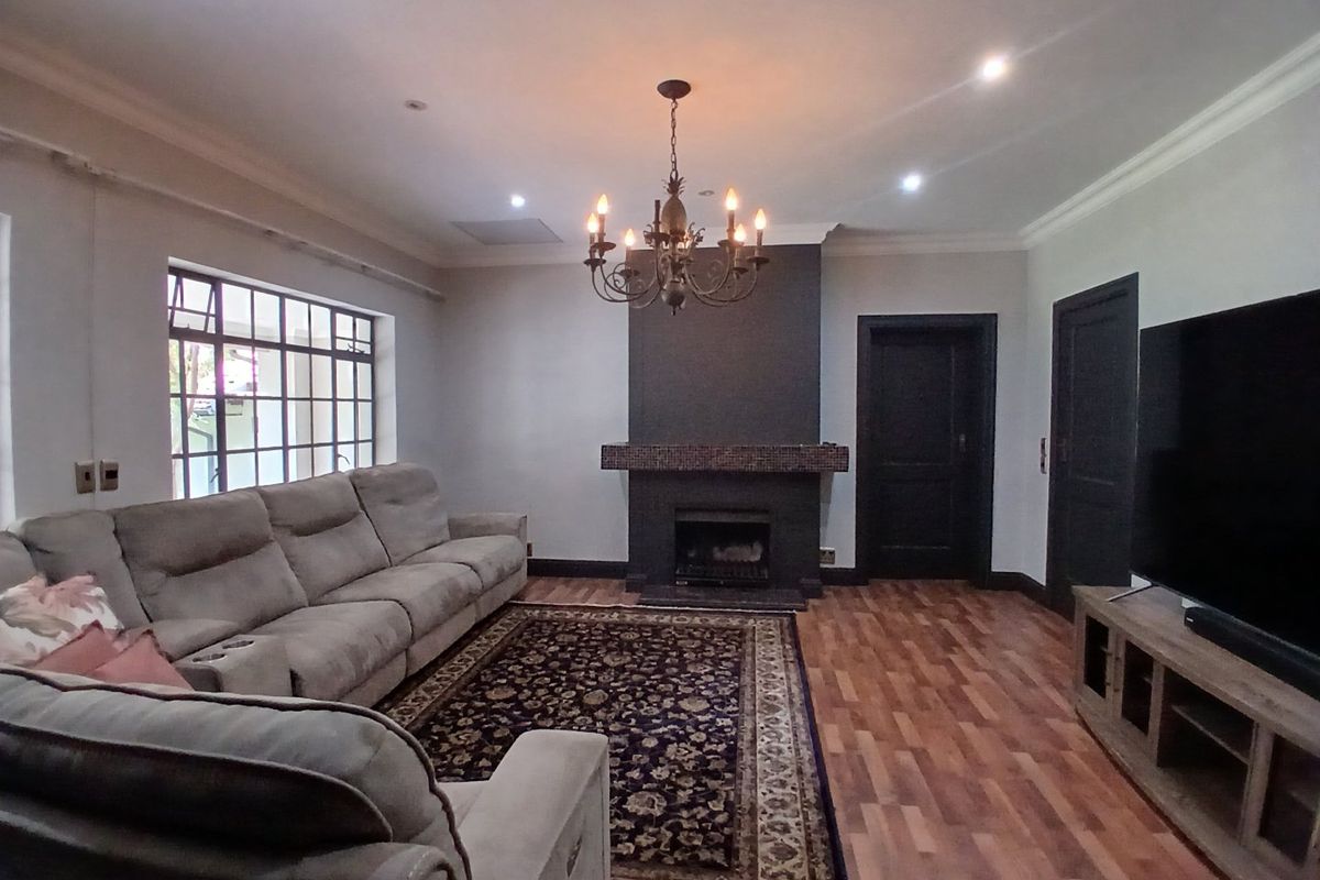 Spacious living room featuring a central fireplace with a dark feature wall, elegant chandelier lighting, and warm laminate flooring.
