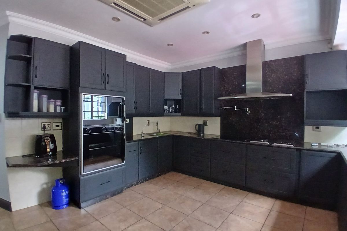 Spacious kitchen featuring dark cabinetry, granite countertops, built-in oven, stainless steel extractor fan, and ceiling-mounted air conditioning.