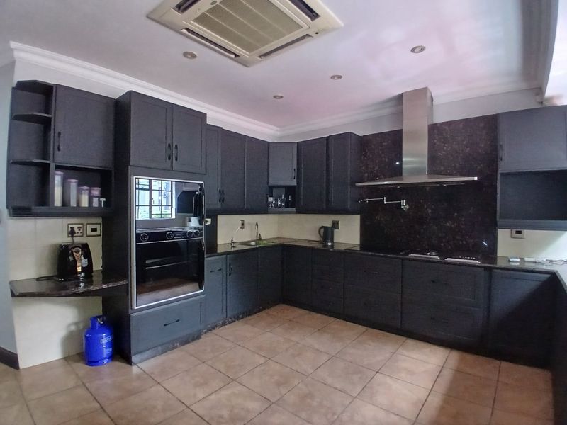 Spacious kitchen featuring dark cabinetry, granite countertops, built-in oven, stainless steel extractor fan, and ceiling-mounted air conditioning.