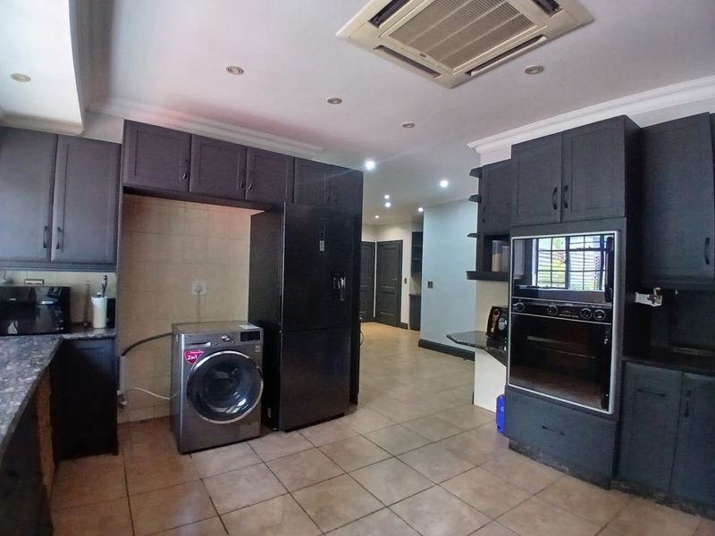 A spacious kitchen featuring dark cabinetry, integrated oven, tiled flooring, and recessed lighting, offering a functional layout with ample storage space.