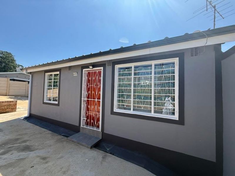 Front elevation of a residential house featuring a grey painted facade, security gates, and security bars on windows.