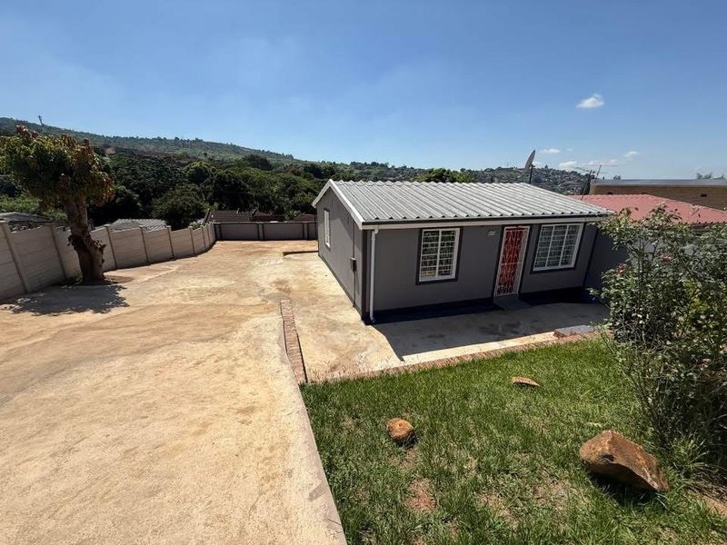 A detached single-story home featuring a corrugated metal roof, secure window bars, and a spacious concrete driveway enclosed by precast boundary walls.