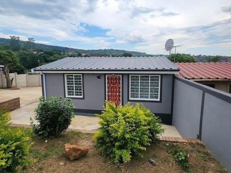 A view of the rear exterior of the house featuring a grey facade, corrugated metal roof, security gate, and a surrounding boundary wall.