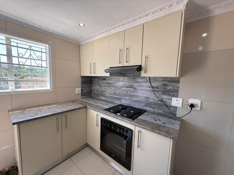 A clean, modern kitchen featuring neutral cabinetry, stone-look laminate countertops, a built-in electric oven and hob, and a stylish tiled backsplash.