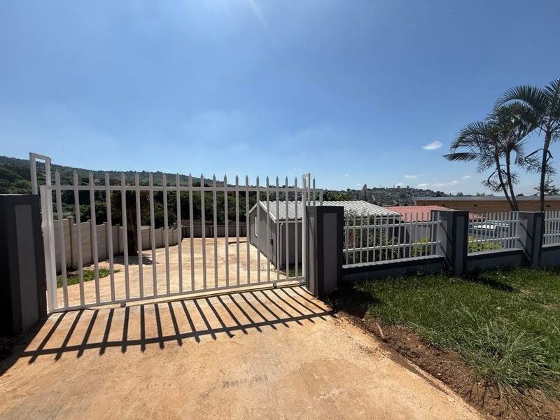 Front view of the property featuring a secure metal gate, concrete perimeter walling, and a paved driveway leading to the main structure.