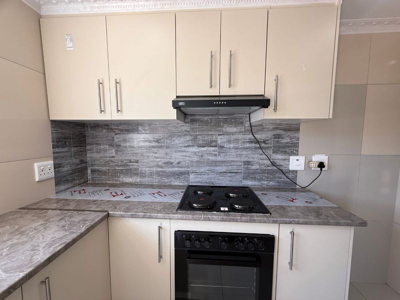 A clean, modern kitchen featuring neutral cabinetry, a stone-look laminate countertop, a tiled backsplash, and integrated cooking appliances.