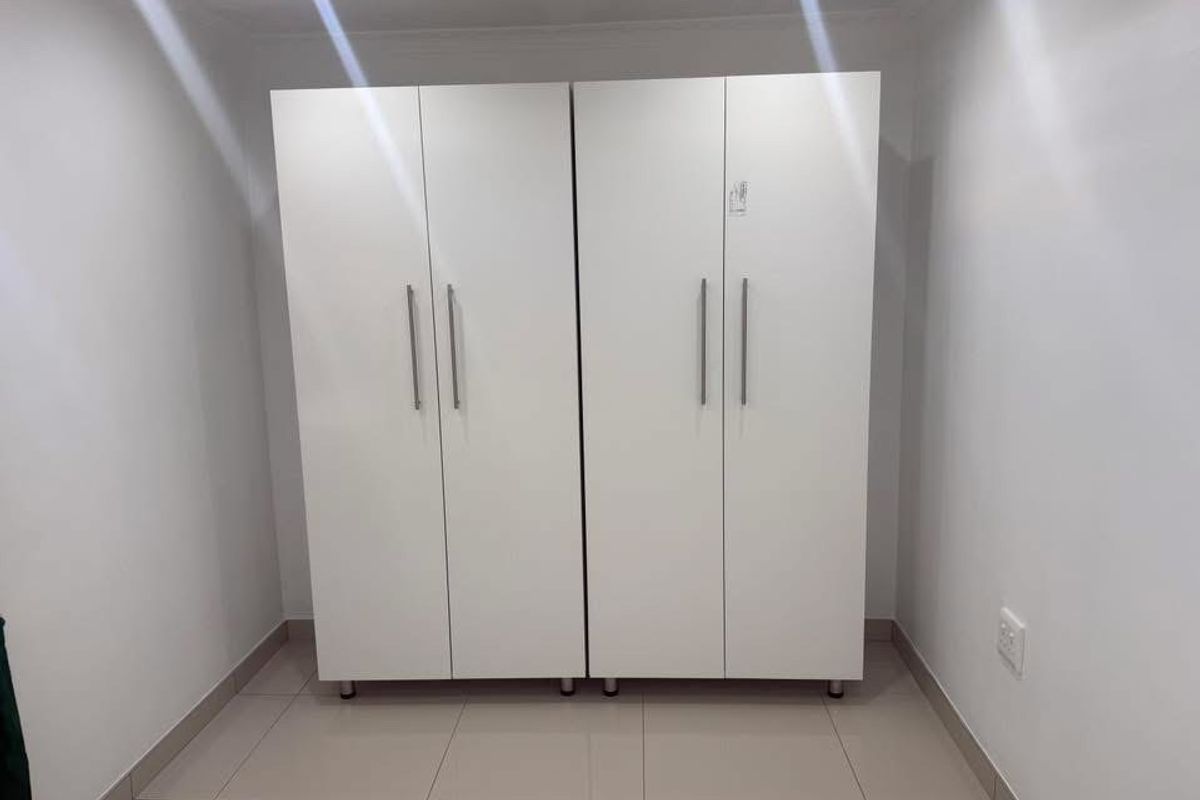 A clean, minimalist bedroom space featuring neutral tiled flooring and modern white built-in cupboards.