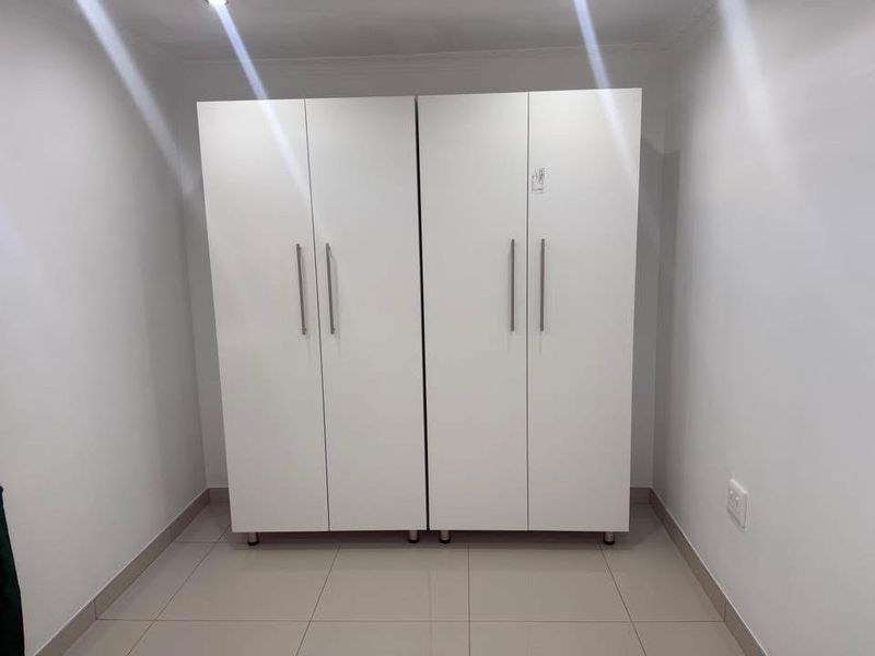 A clean, minimalist bedroom space featuring neutral tiled flooring and modern white built-in cupboards.