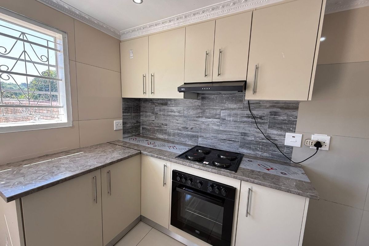 A clean, modern kitchen featuring neutral cabinetry, stone-look laminate countertops, a built-in oven with hob, and a stylish tiled backsplash.