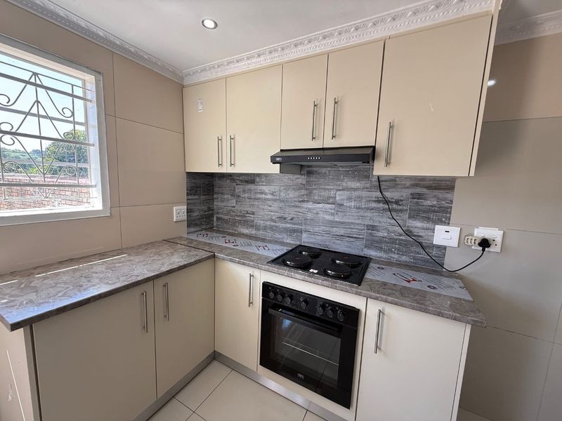 A clean, modern kitchen featuring neutral cabinetry, stone-look laminate countertops, a built-in oven with hob, and a stylish tiled backsplash.