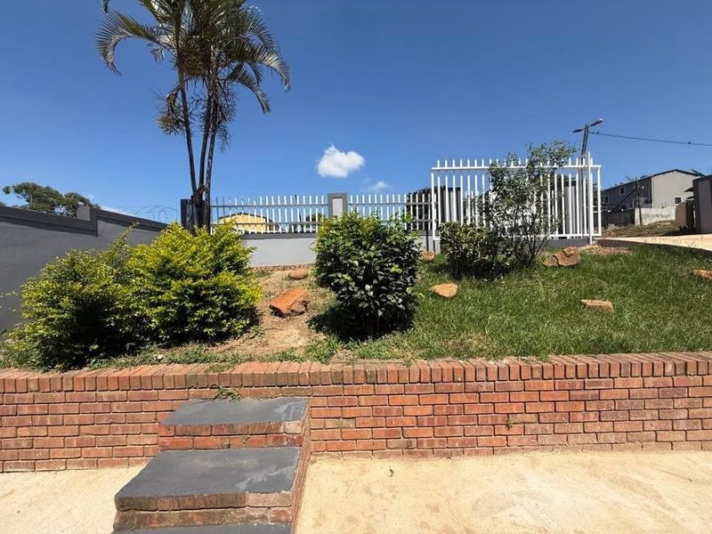 A landscaped garden area featuring a brick retaining wall, stone steps, and metal security fencing.