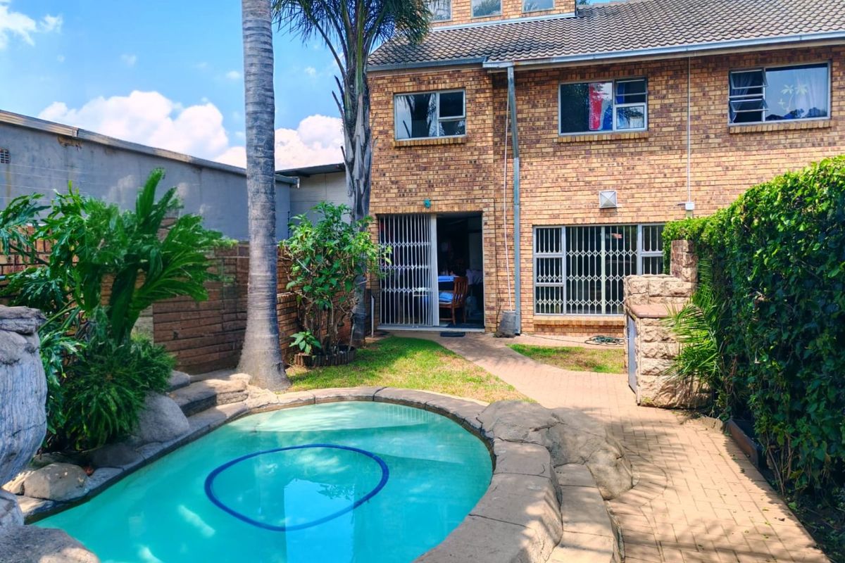 Rear view of a brick house featuring a swimming pool, paved patio area, and established garden landscaping.