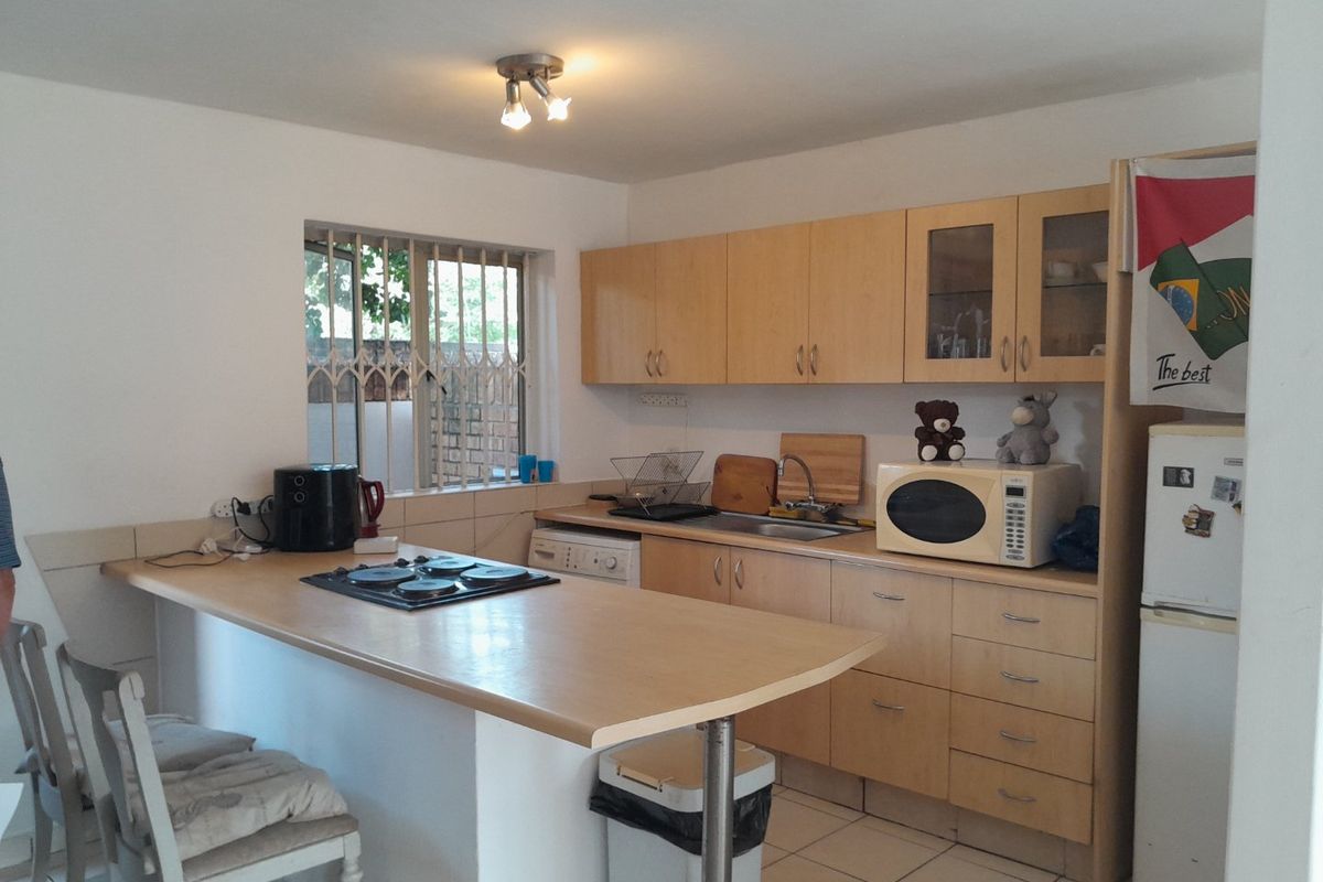 Functional kitchen featuring light wood cabinetry, a breakfast bar with integrated hob, tiled flooring, and a window with security bars.