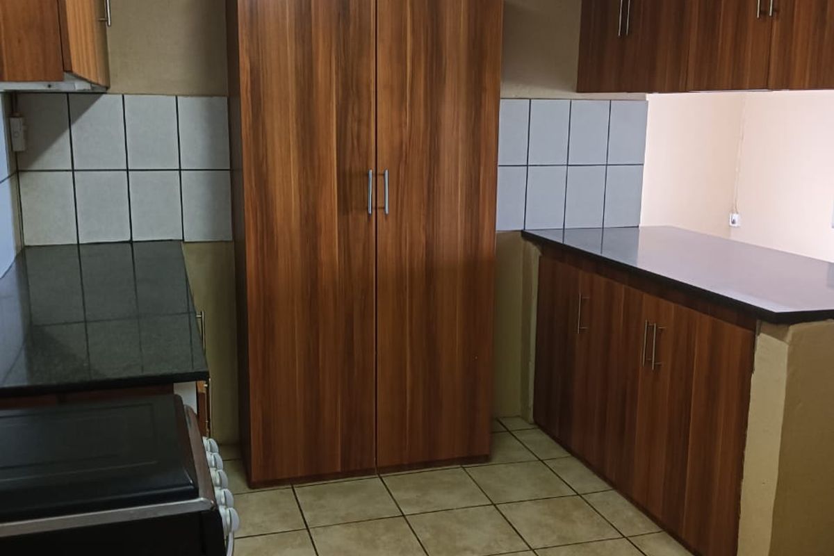 Functional kitchen featuring wood-look cabinetry, dark countertops, tiled backsplash, and ceramic floor tiles, providing a practical workspace.
