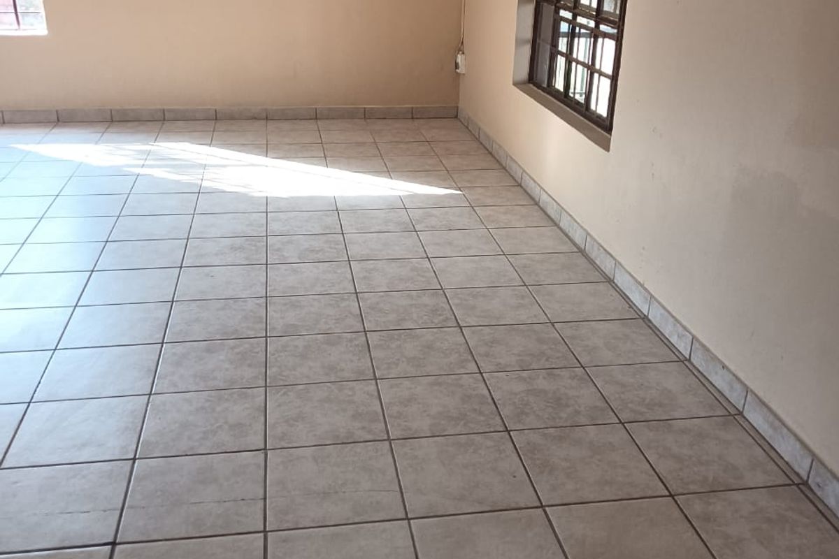 A spacious, empty living area featuring neutral ceramic floor tiles and large windows, providing a blank canvas for interior design.