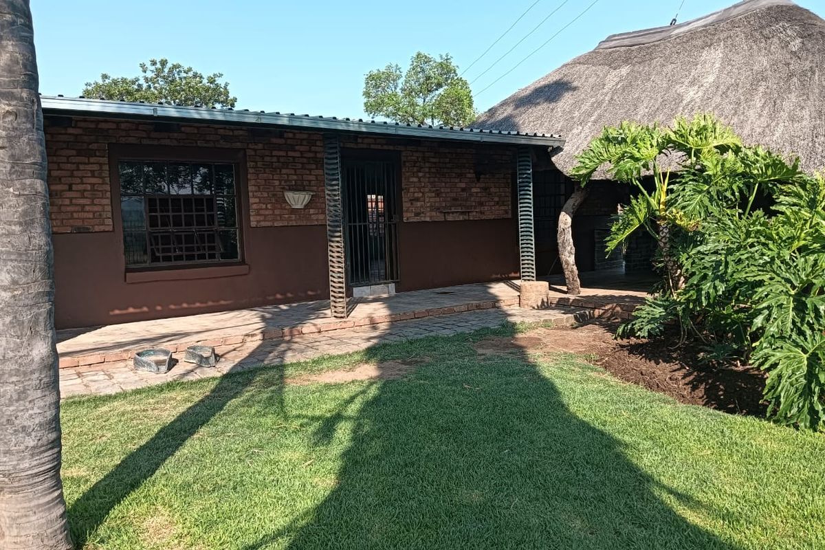 Exterior view of a farm-style dwelling featuring a brick facade, covered patio area, and a traditional thatched roof section.