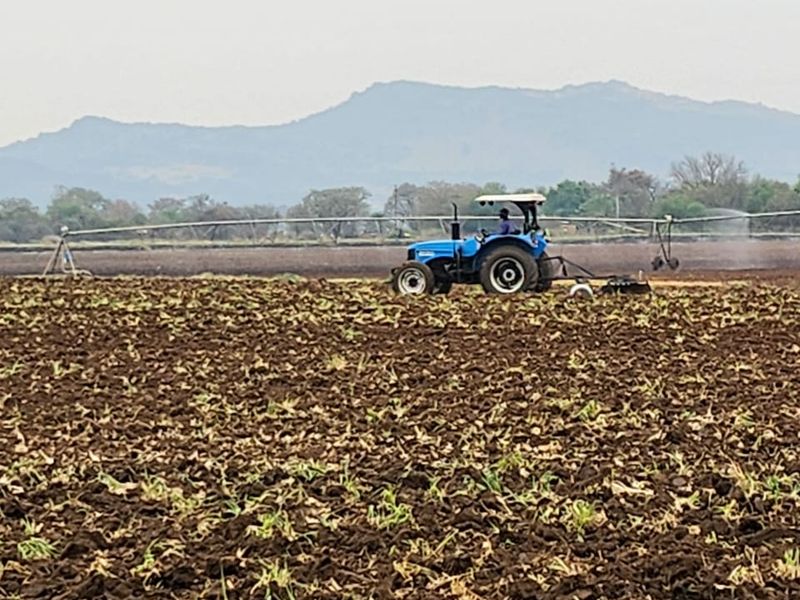 Expansive agricultural farmland featuring a center pivot irrigation system and a tractor working the soil with mountain views in the background.