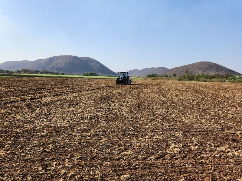 Expansive agricultural farmland featuring tilled soil, set against a scenic backdrop of rolling hills and clear blue skies.