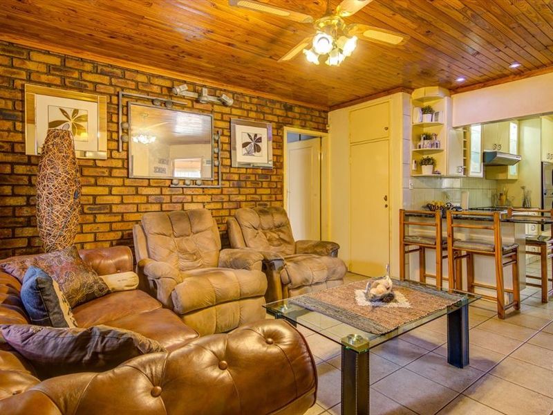 Open-plan living and kitchen area featuring exposed brick walls, timber ceiling, tiled floors, and a functional kitchen with built-in appliances and breakfast bar.