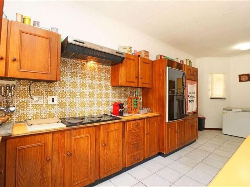 A functional kitchen featuring traditional wooden cabinetry, an integrated oven, an electric hob with an extractor fan, and tiled flooring.