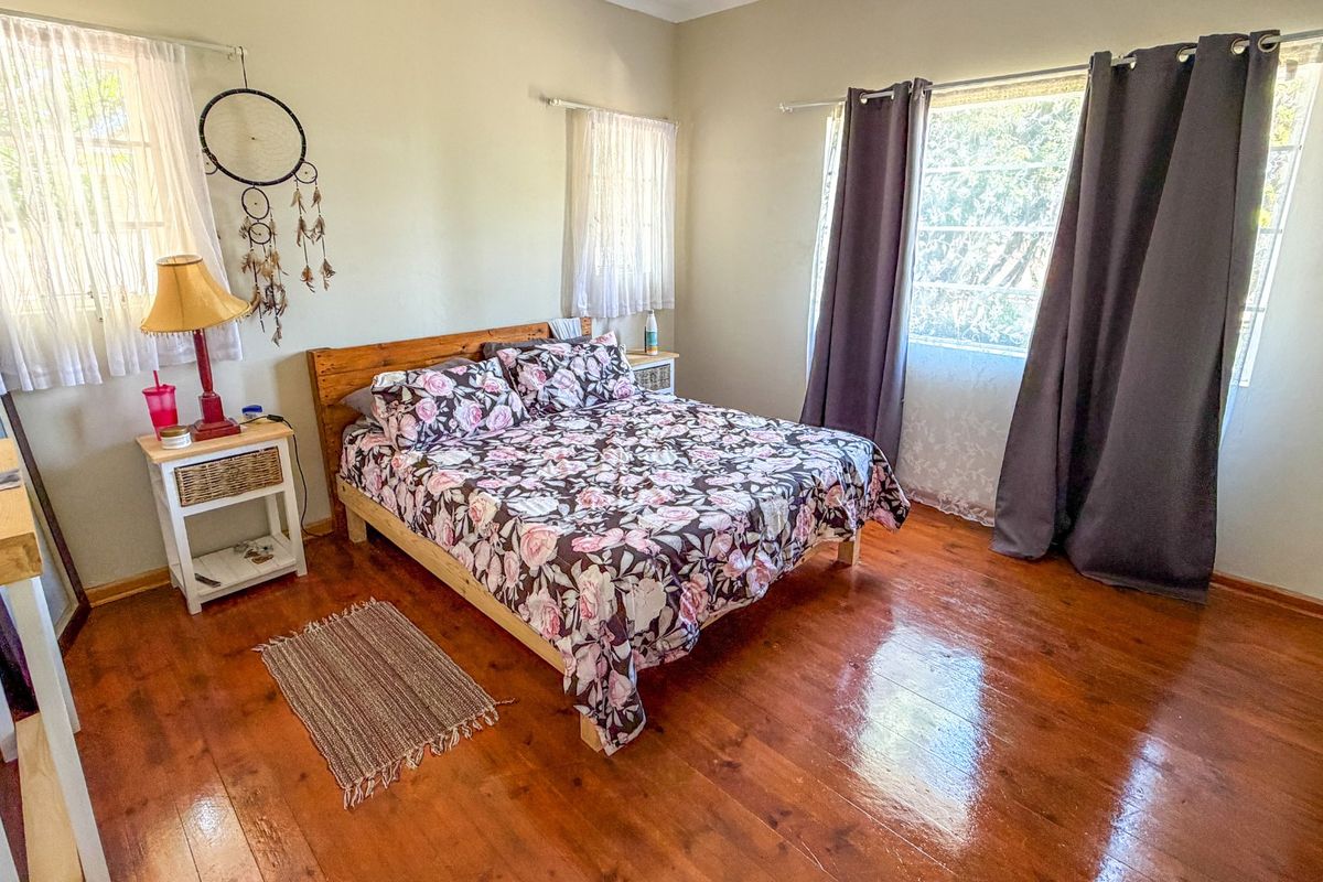 A bedroom featuring polished hardwood flooring and dual windows with curtain rods, providing natural light and a warm atmosphere.
