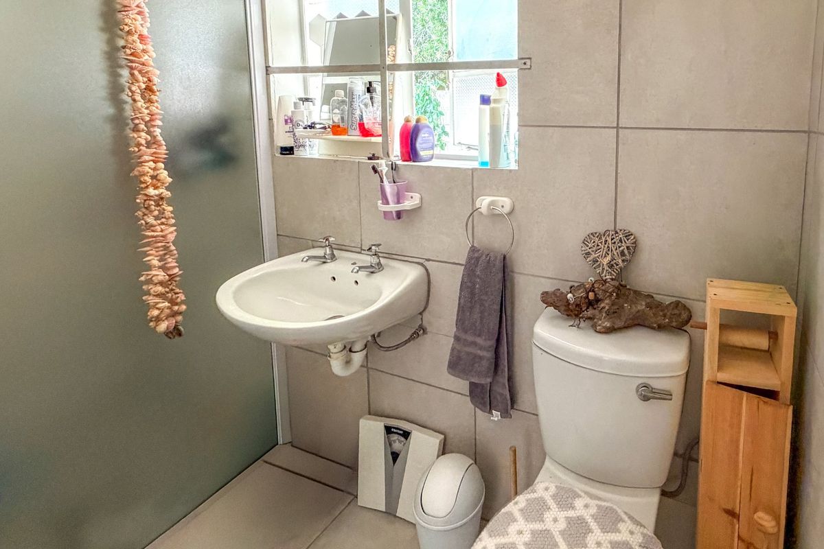 A functional bathroom featuring a wall-mounted basin, close-coupled toilet, and a frosted glass shower screen with neutral ceramic tiling throughout.