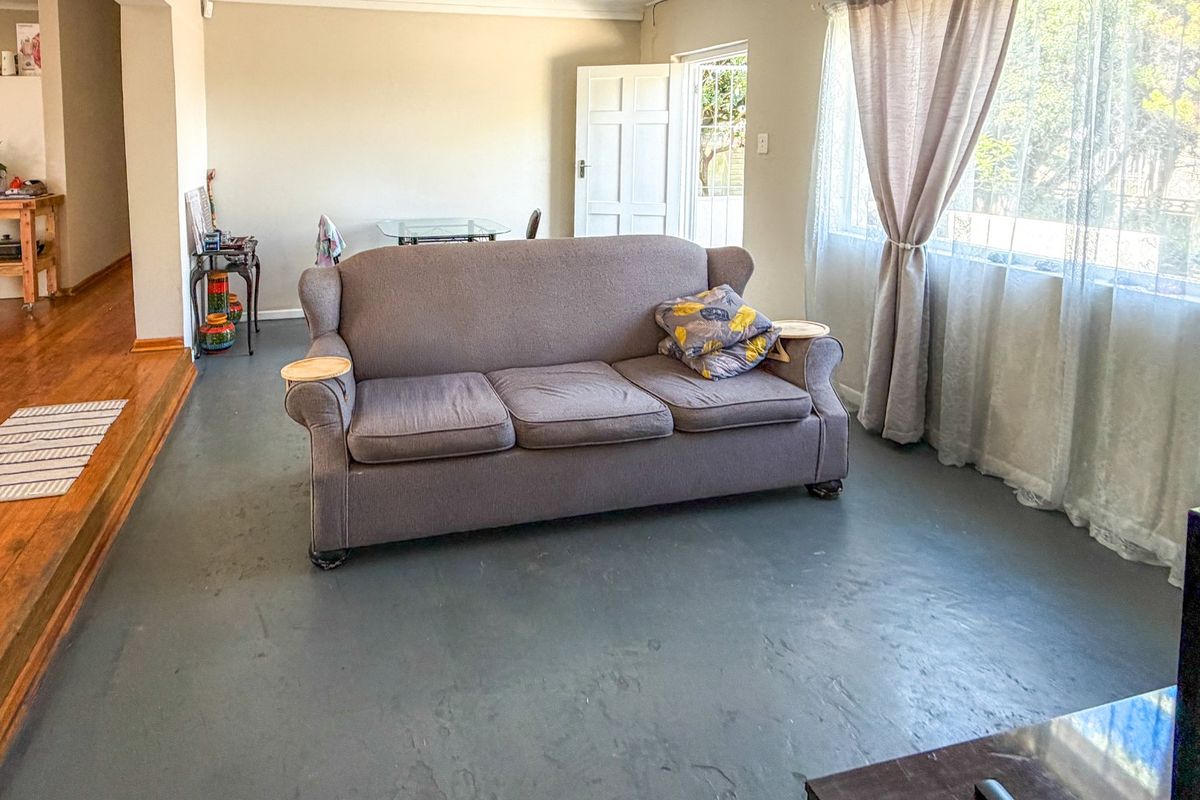 A living room area featuring a mix of painted concrete and timber flooring, with access to an exterior door and natural light.